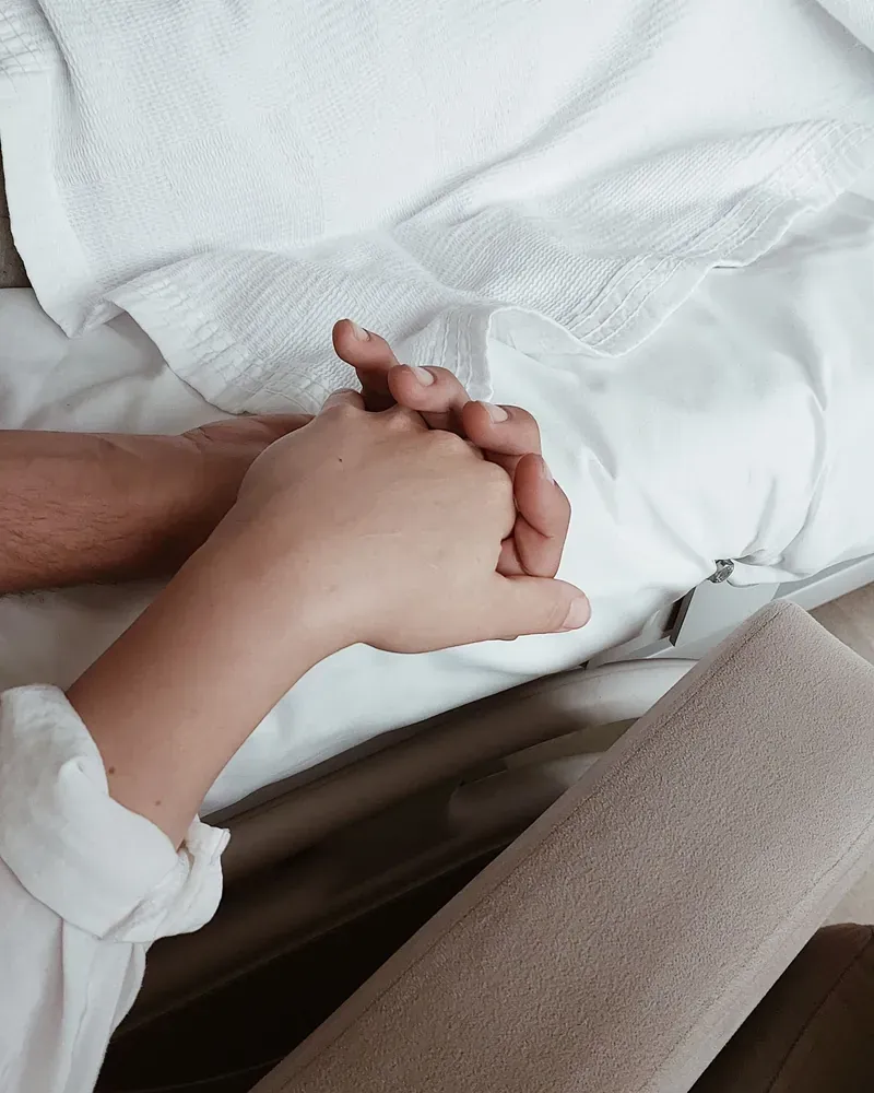 Two hands clasped on white bedding