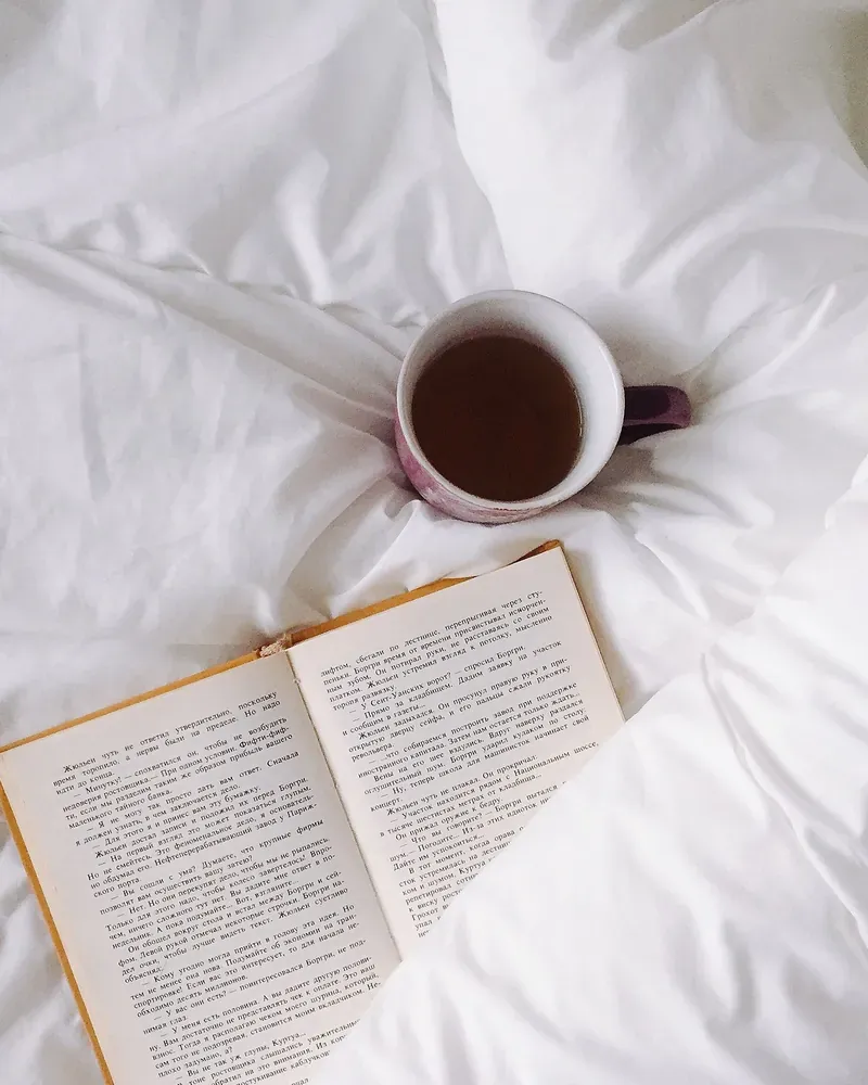 Open book and a cup of tea on white bedding