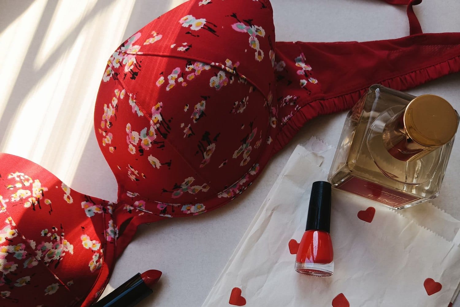 Red floral bra with perfume, red nail polish and paper hearts