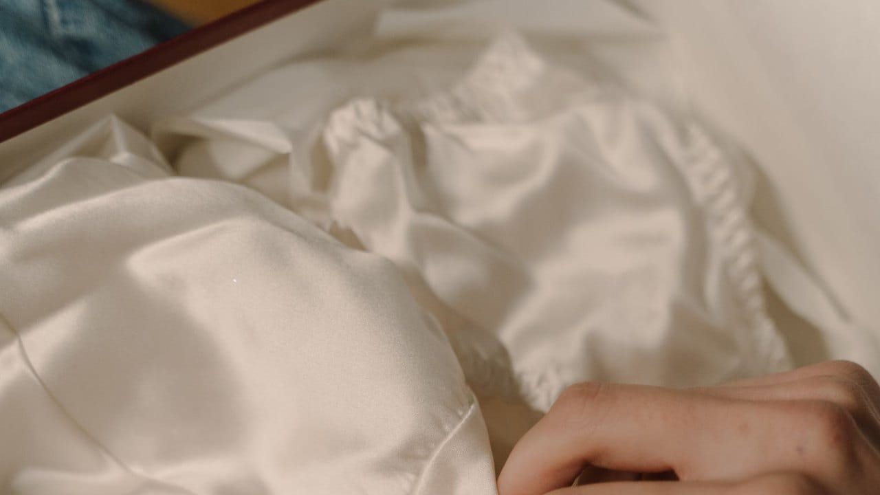 Hands unwrapping ivory silk lingerie from a gift box