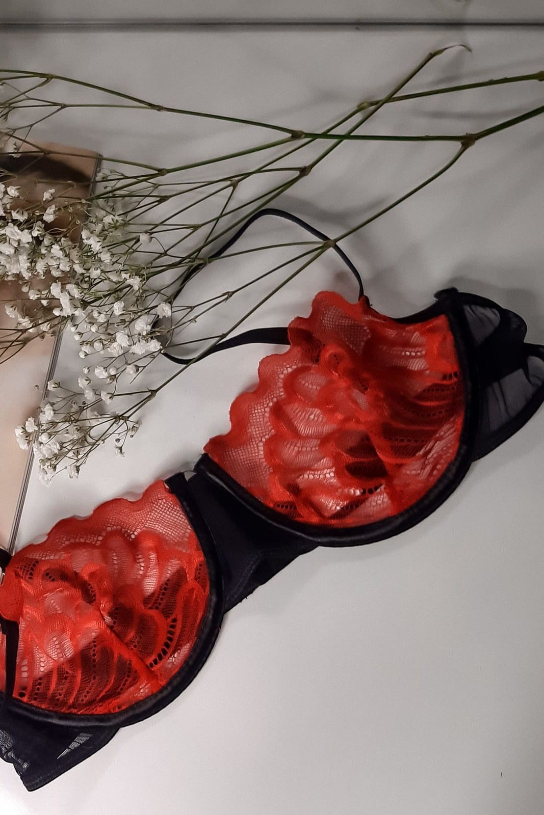Red and black lace bra on a white surface with dried gypsophila