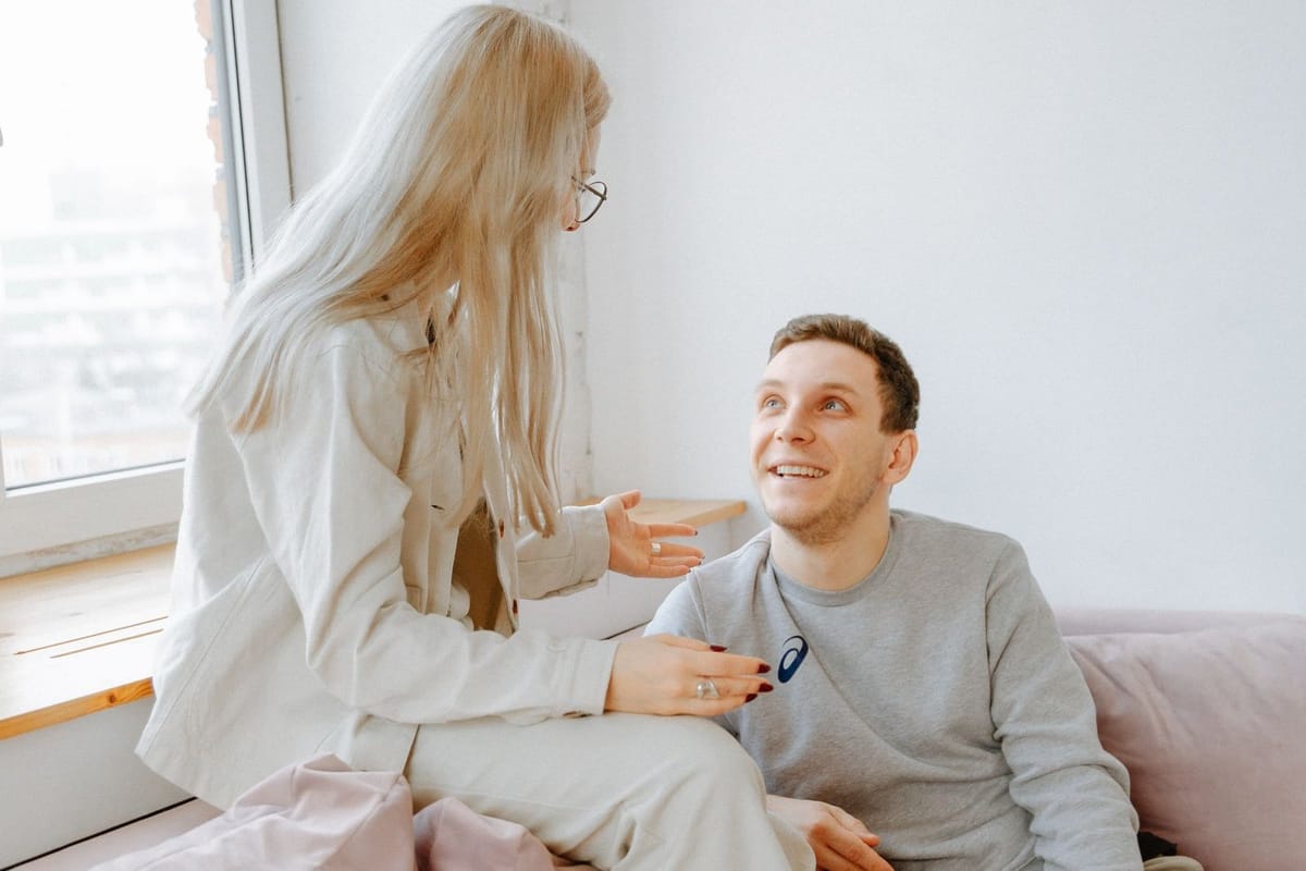 A smiling couple chatting on a pink sofa by a sunny window