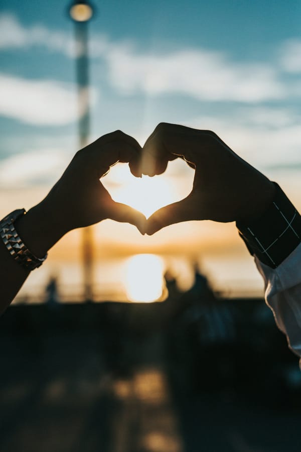 Couple hands forming a heart at sunset