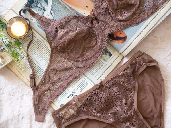 Mocha lace bra and matching brief laid flat on a magazine beside a lit candle
