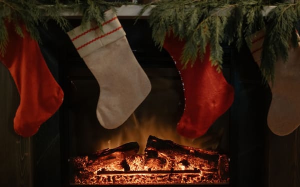 Red and cream Christmas stockings hanging from a pine-garlanded mantel above a glowing fire