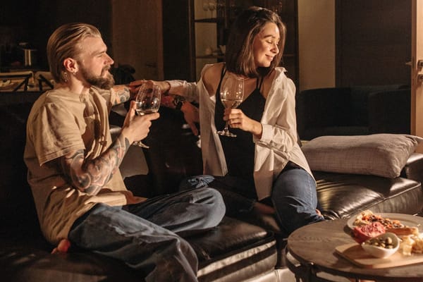 A couple clinking wine glasses on a leather sofa in a warm, softly lit living room