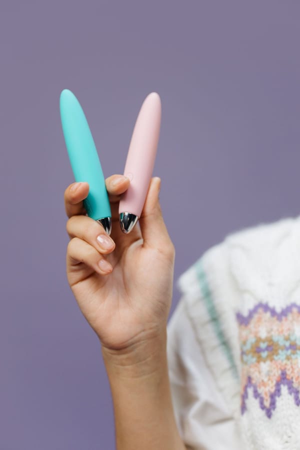 Hand holding two slim, pocket-sized vibrators in mint and blush